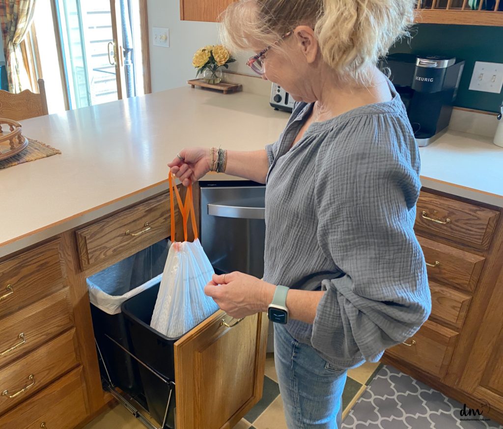 a woman pulling out a full trash bag from the can in a kitchen 
