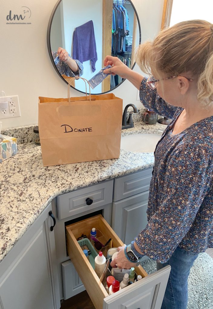 a woman putting lotion into a donation bag in a bathroom