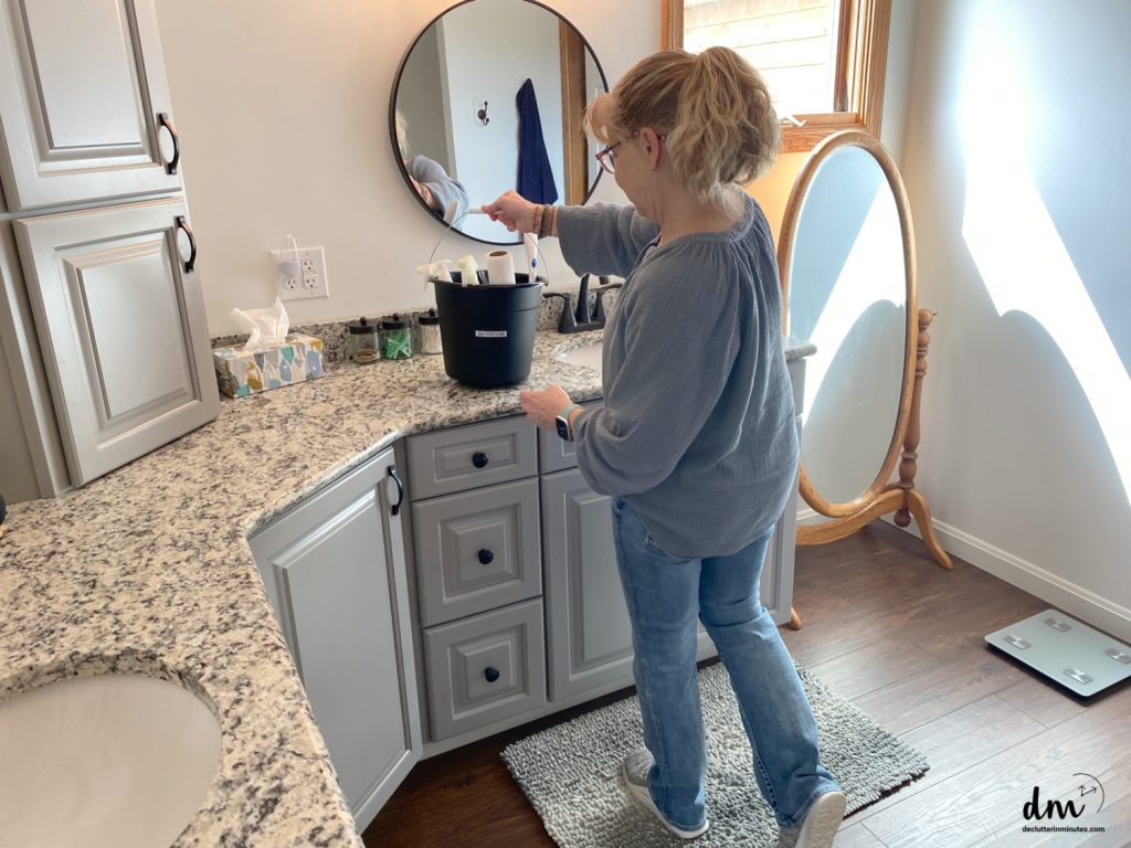 a woman setting a black cleaning bucket on the sink in a bathroom
