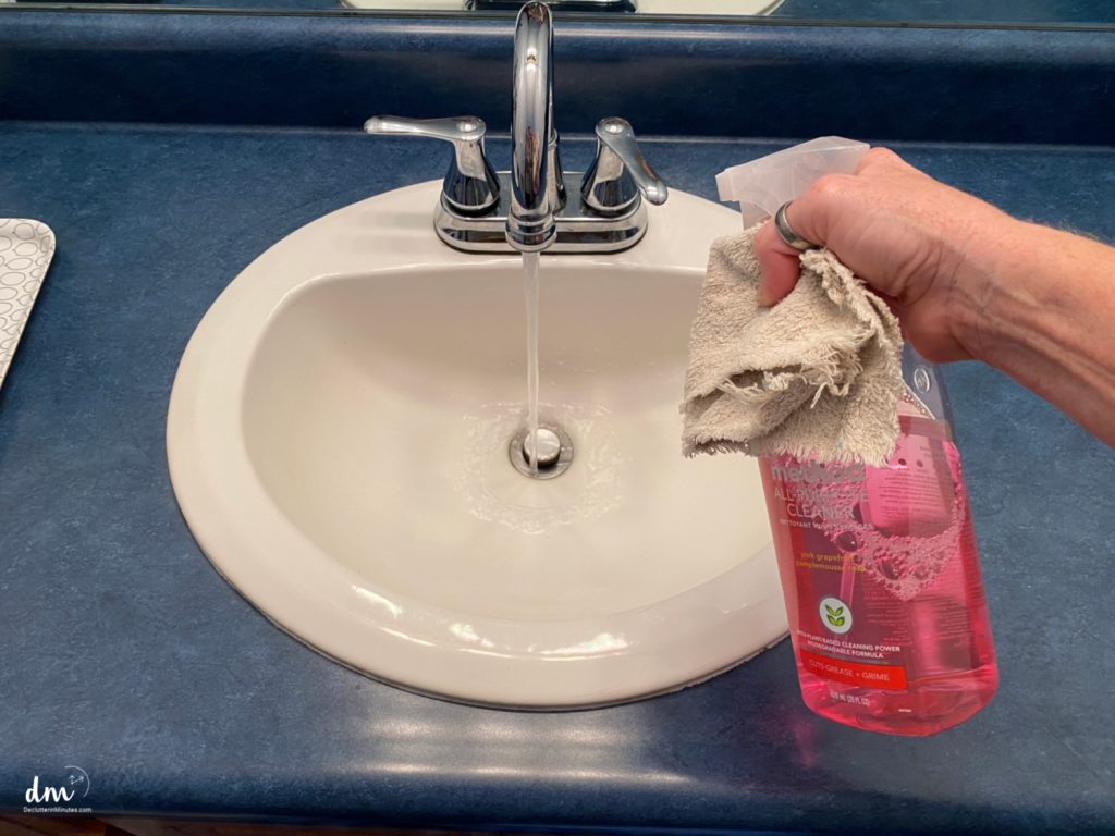 hands spraying cleaner into a bathroom sink with the water running