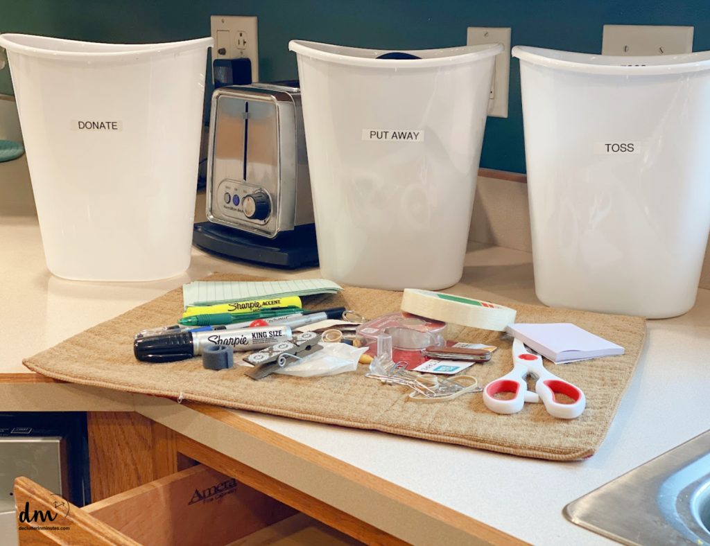 3 labeled buckets in front of a pile of clutter on a kitchen counter