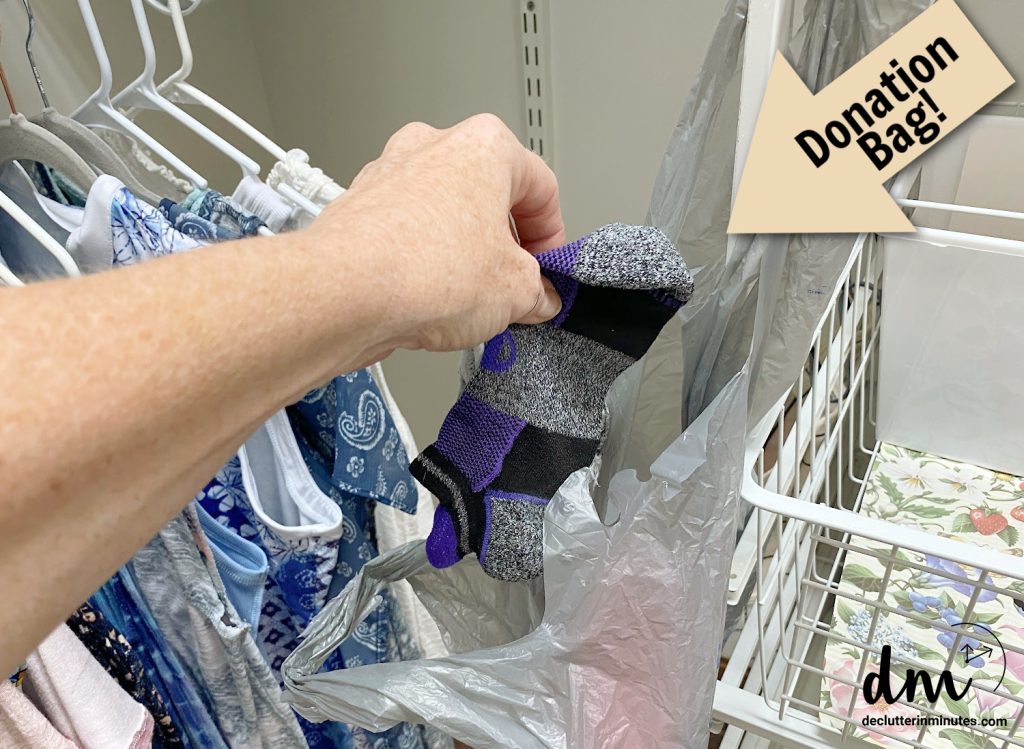 a hand putting socks into a plastic bag in a closet 