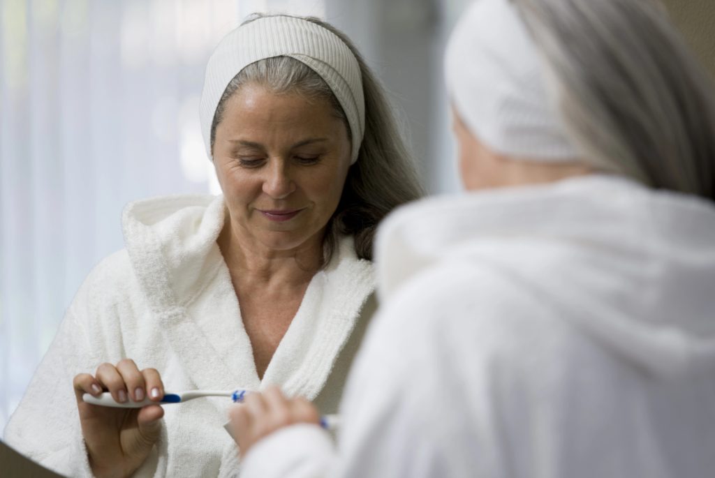 a midlife woman brushing her teeth as a daily habit