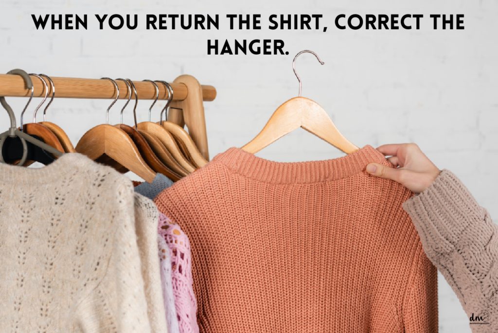 a woman holding a peach colored sweater on a wooden hanger