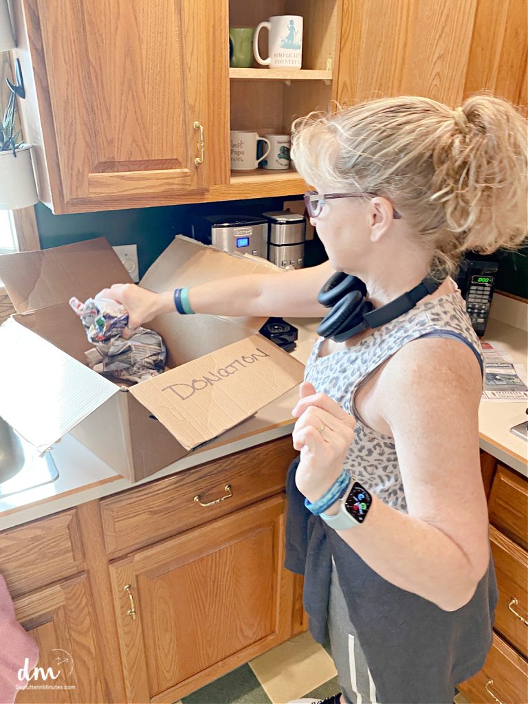 a woman putting a coffee cup into a donation box near to a cabinet in a kitchen