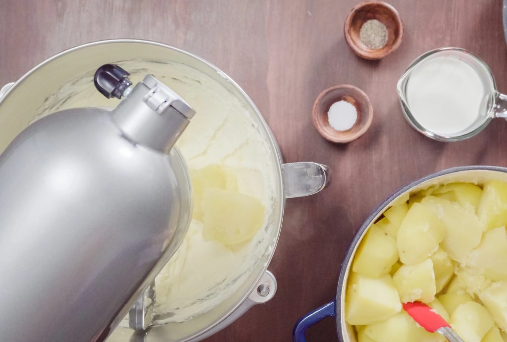 potatoes in a bowl next to a mixer of mashed potatoes