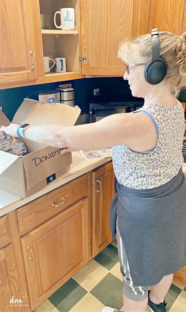 woman with headphones on decluttering a kitchen cabinet 
