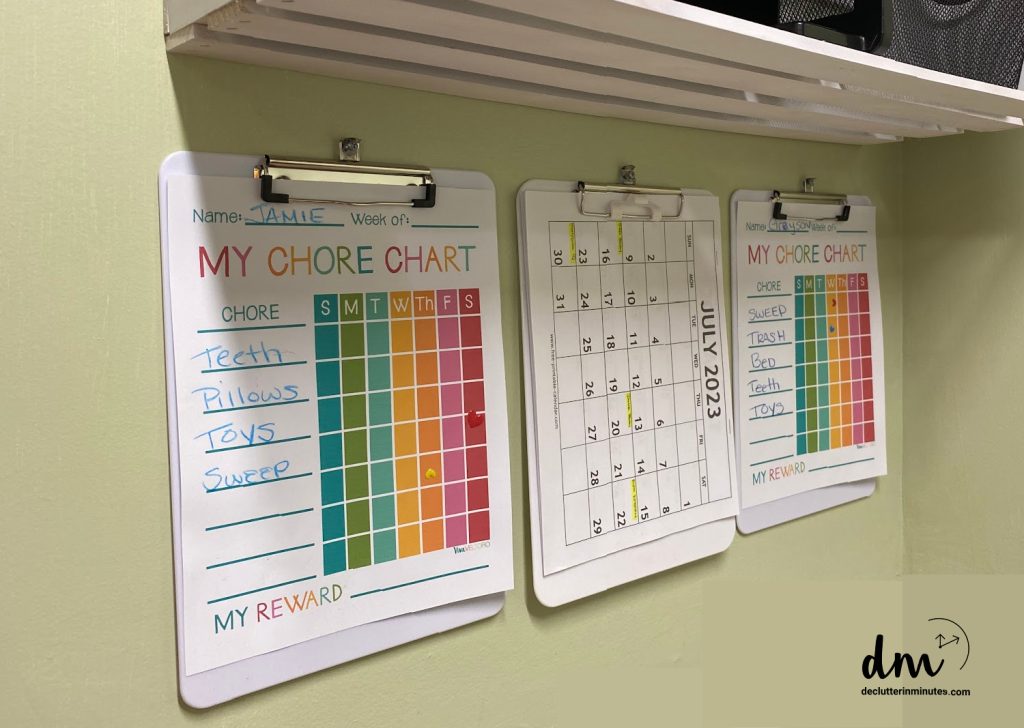 3 clipboards holding colorful chore charts and a calendar hanging in a home hub set up