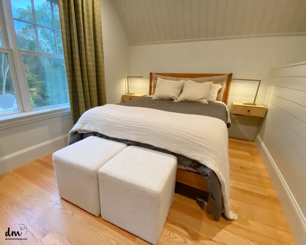 a bed in a room that is neutral, with white ottomans at the food