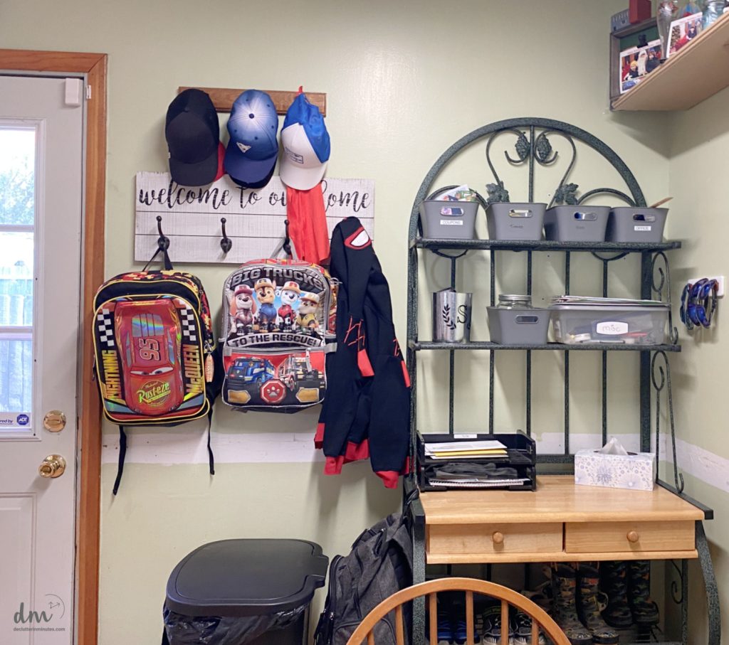 a home hub near to a door in a home with book bags hanging and grey baskets labeled on a shelf