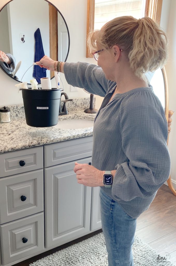 a woman setting a cleaning bucket on the sink of a bathroom 