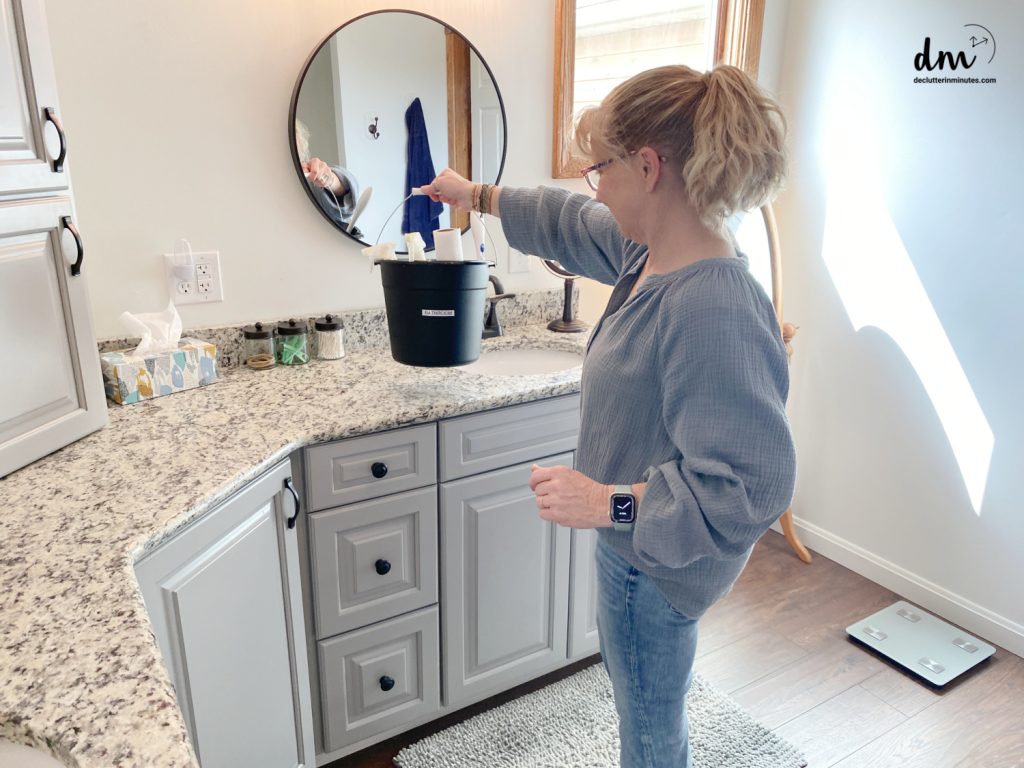 a woman with a black bucket of cleaning supplies in a bathroom