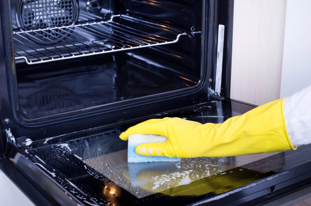 hands cleaning the door of an oven