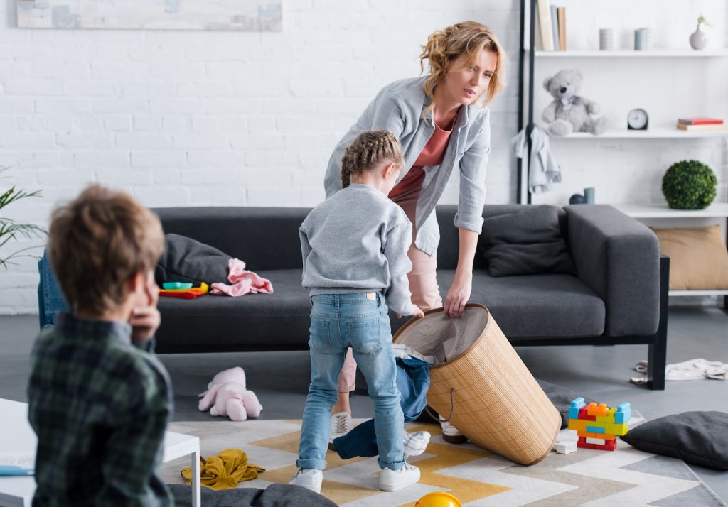 tired mom cleaning a family room with her kids playing nearby 