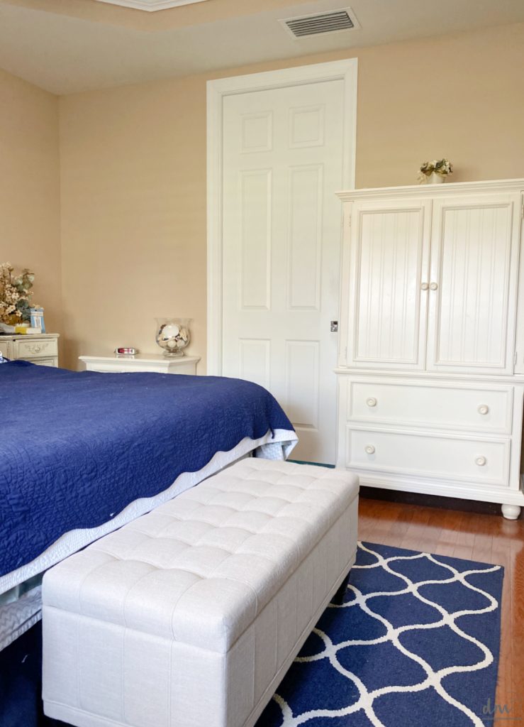 a white storage ottoman at the foot of a blue bed 