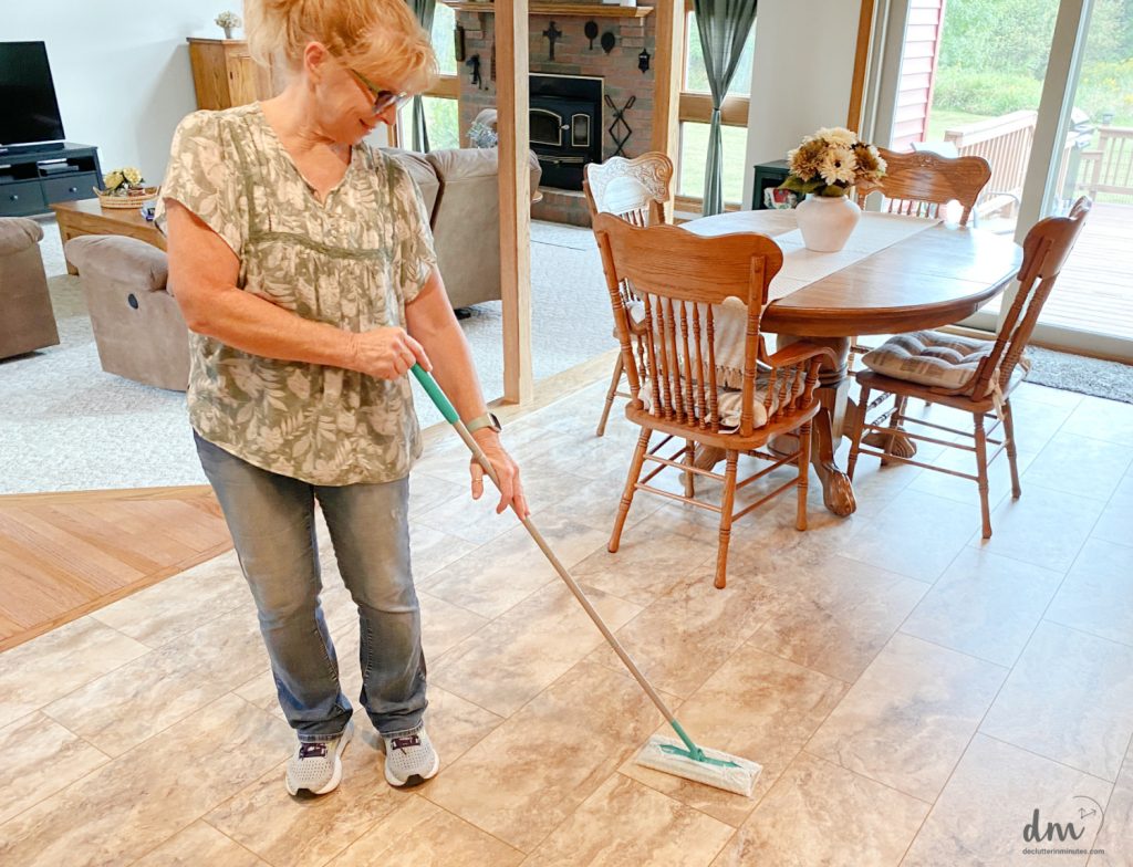 a woman cleaing a floor in a kitchen with a duster mop 
