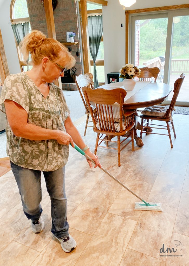 A woman mopping the tile floor in a cozy dining area with wooden furniture and a vase of flowers on the table