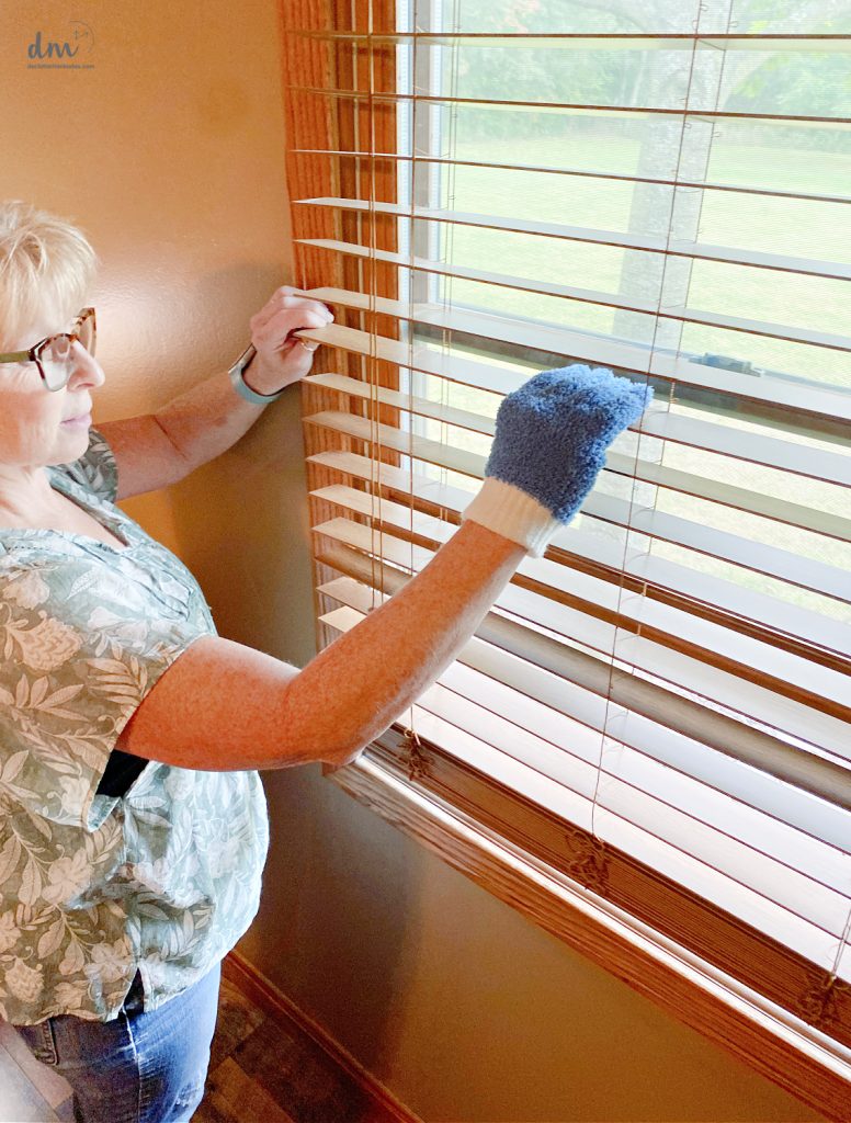 a woman using a dusting glove to clean a blind in a bedroom 