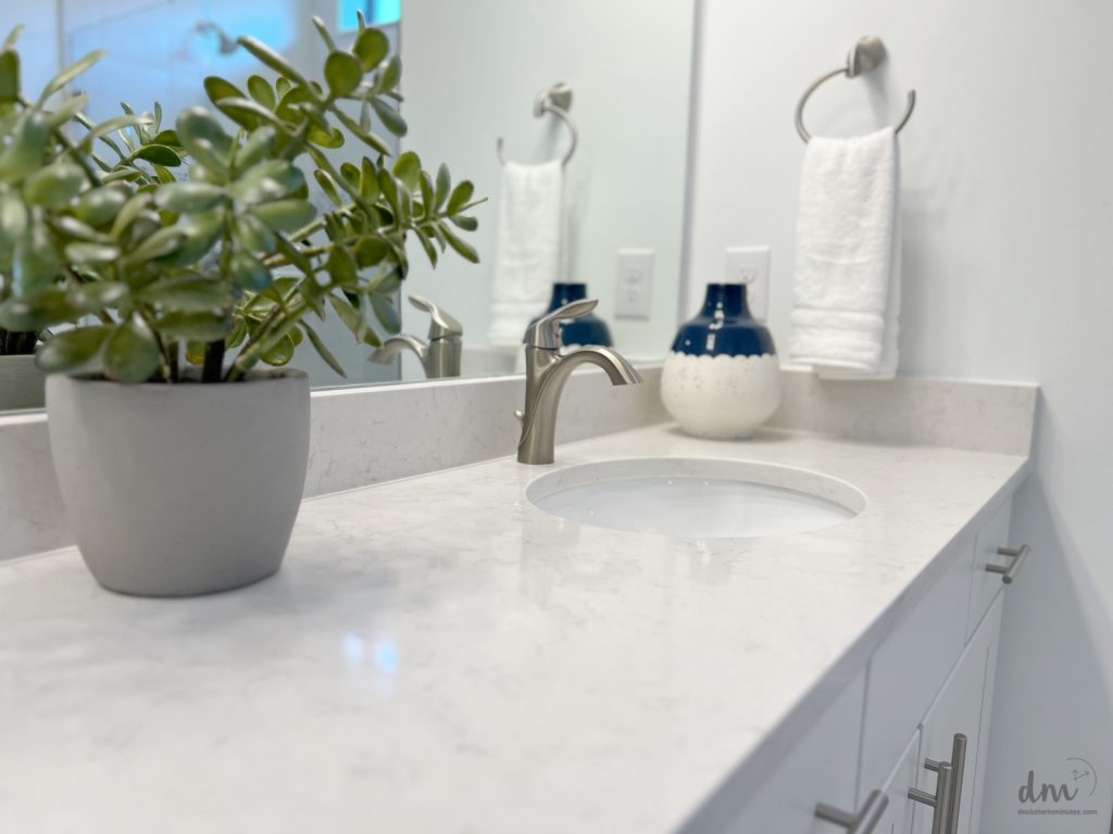 A bathroom with a white marble countertop, a silver faucet, a potted plant, and neatly folded towels on towel rings