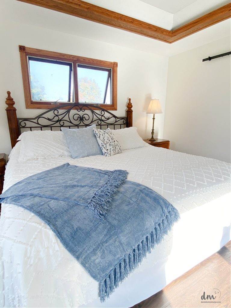 a white bed with a blue blanket and pillows in a bedroom