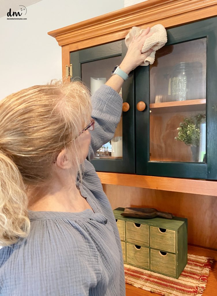 a woman cleaning a green and brown china cabinet with a rag