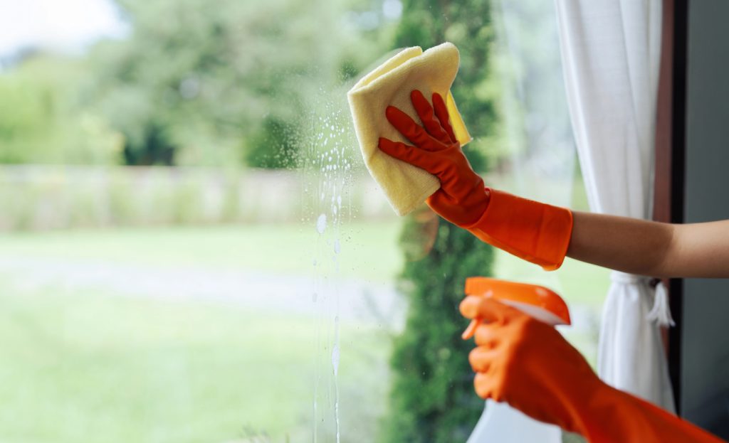 hands cleaning a window in a home