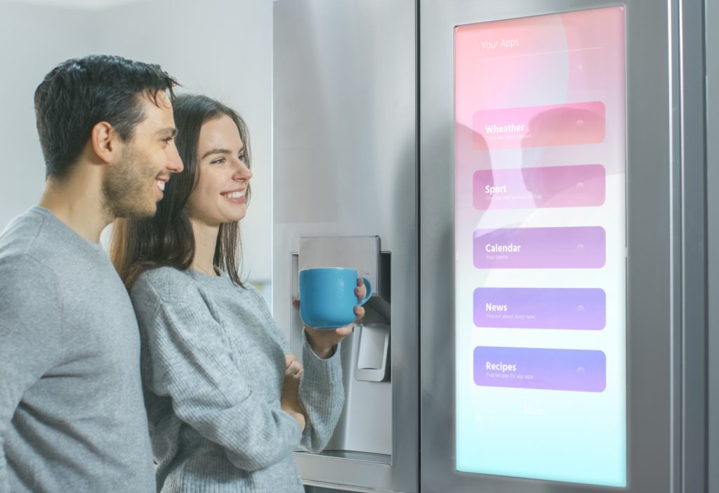 a couple looking at a computer screen on the front of a fridge