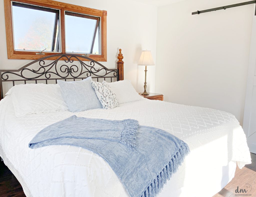 a white bed with a blue blanket at the foot and a few decorative pillows