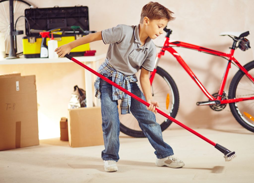 kid sweeping a garage with a push broom