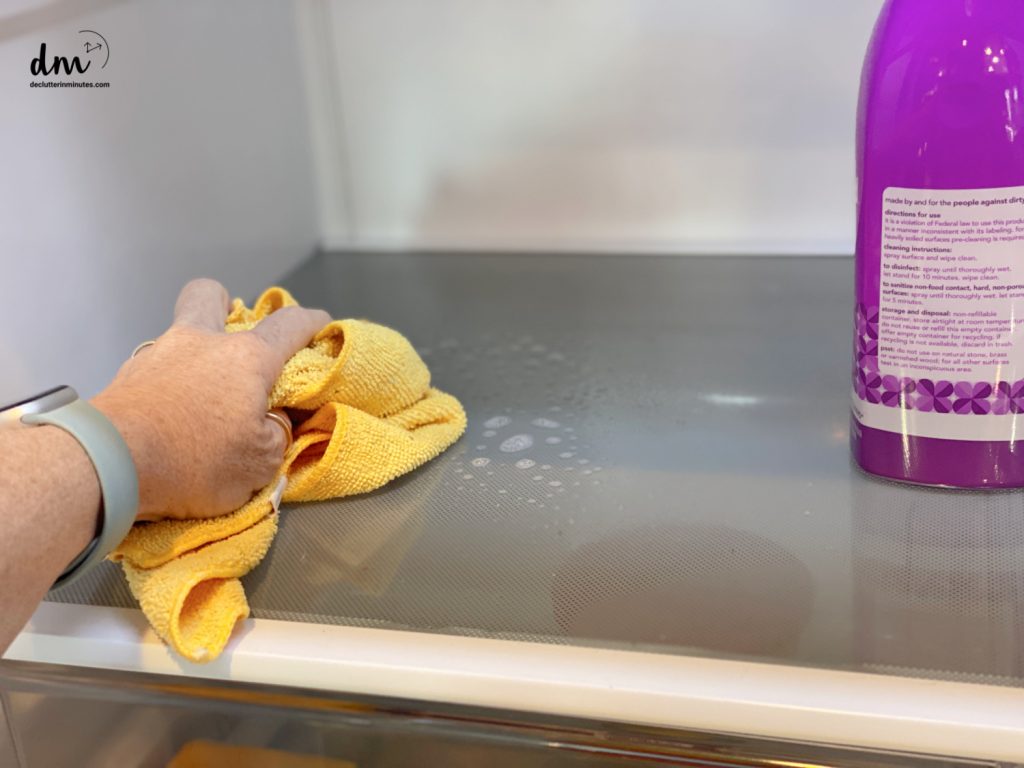 a hand cleaning off a shelf in a refrigerator
