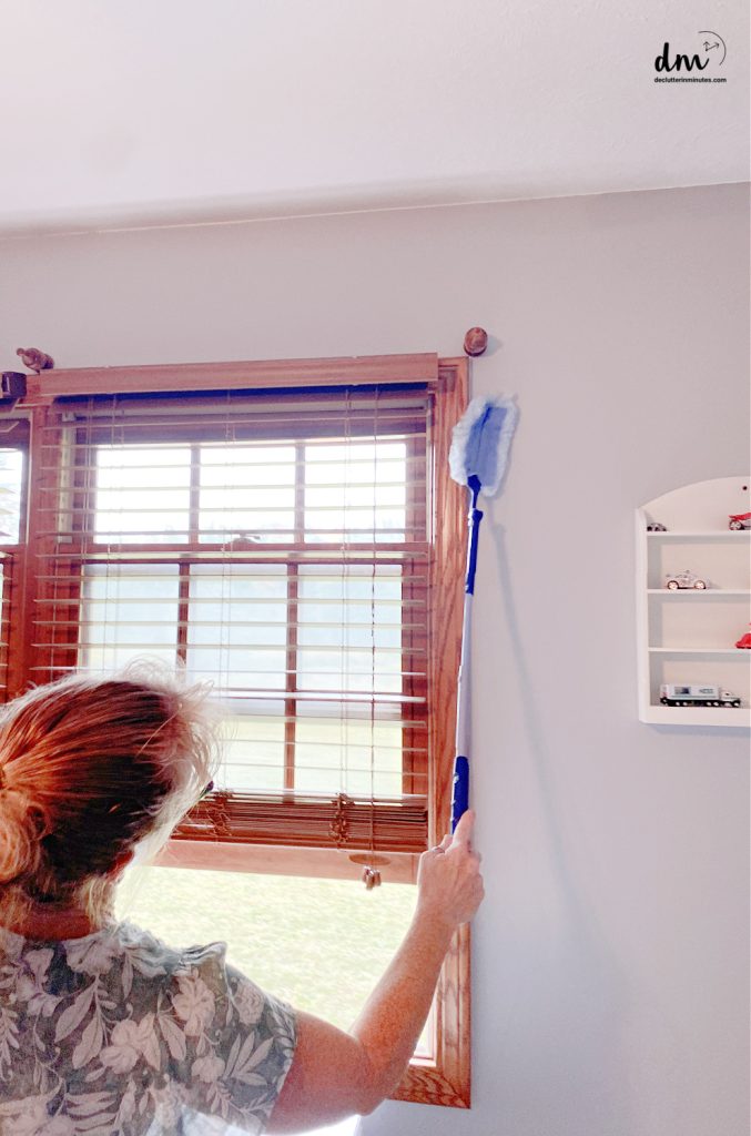 a woman dusting a window frame with a wand duster 