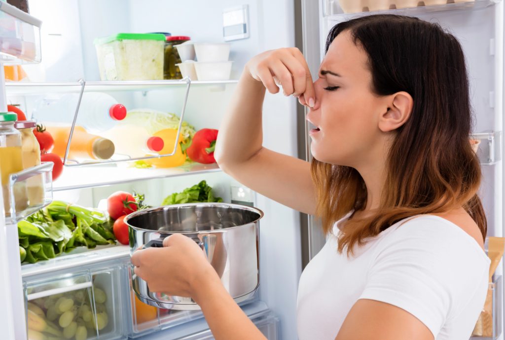 a woman smelling old leftovers with fingers on her nose