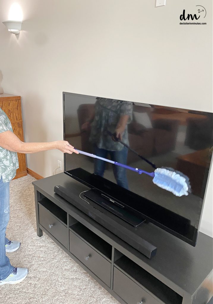 a woman using a duster to clean the front of a TV
