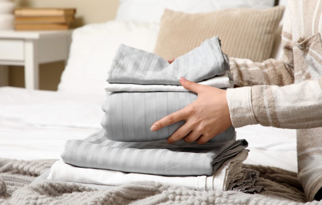 hands holding fresh sheets on a bed to be made