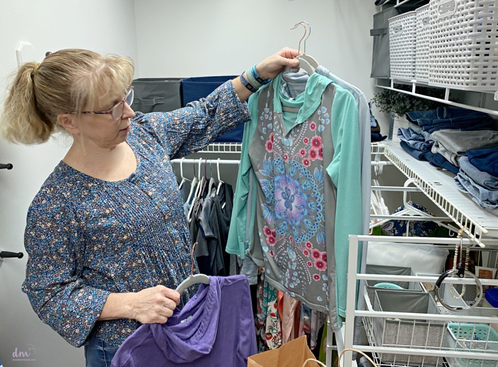 a woman holding up a shirt on a hanger looking at it