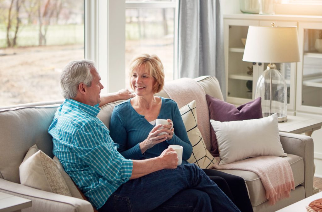 a midlife couple sitting on a couch talking with coffee
