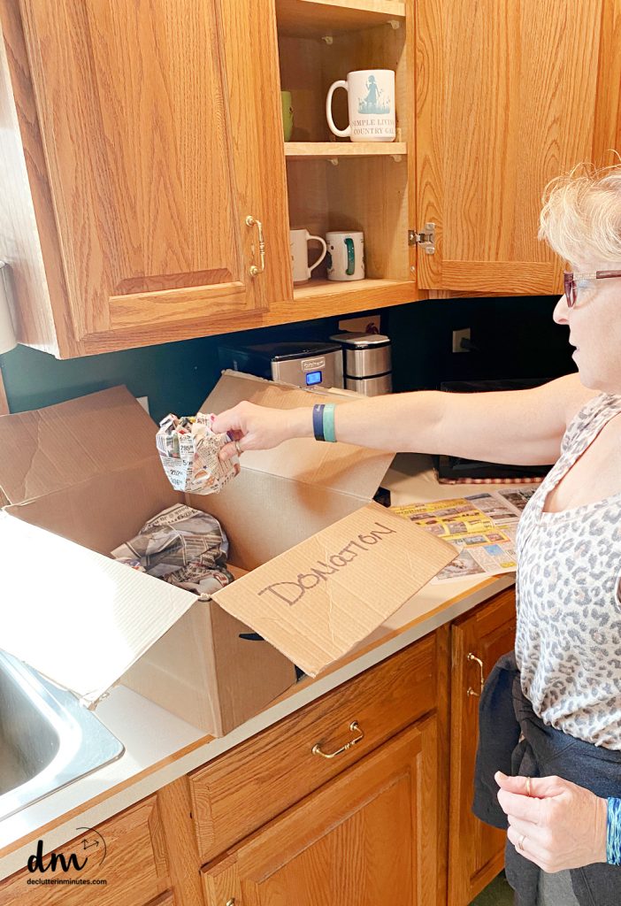 a woman putting mugs into a donation box of a kitchen