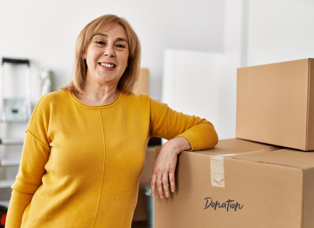 Middle age woman smiling happy standing next to donation boxes