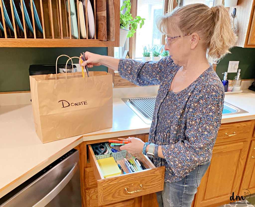 a woman putting pens into a donation bag in a kitchen