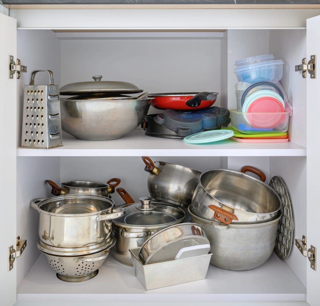 a stuffed and cluttered kitchen cabinet full of pots and pans