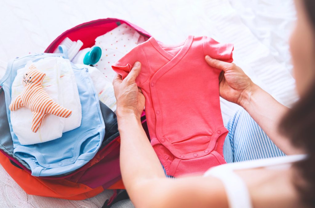 a woman looking at a pink baby onesie over a stack of clothes