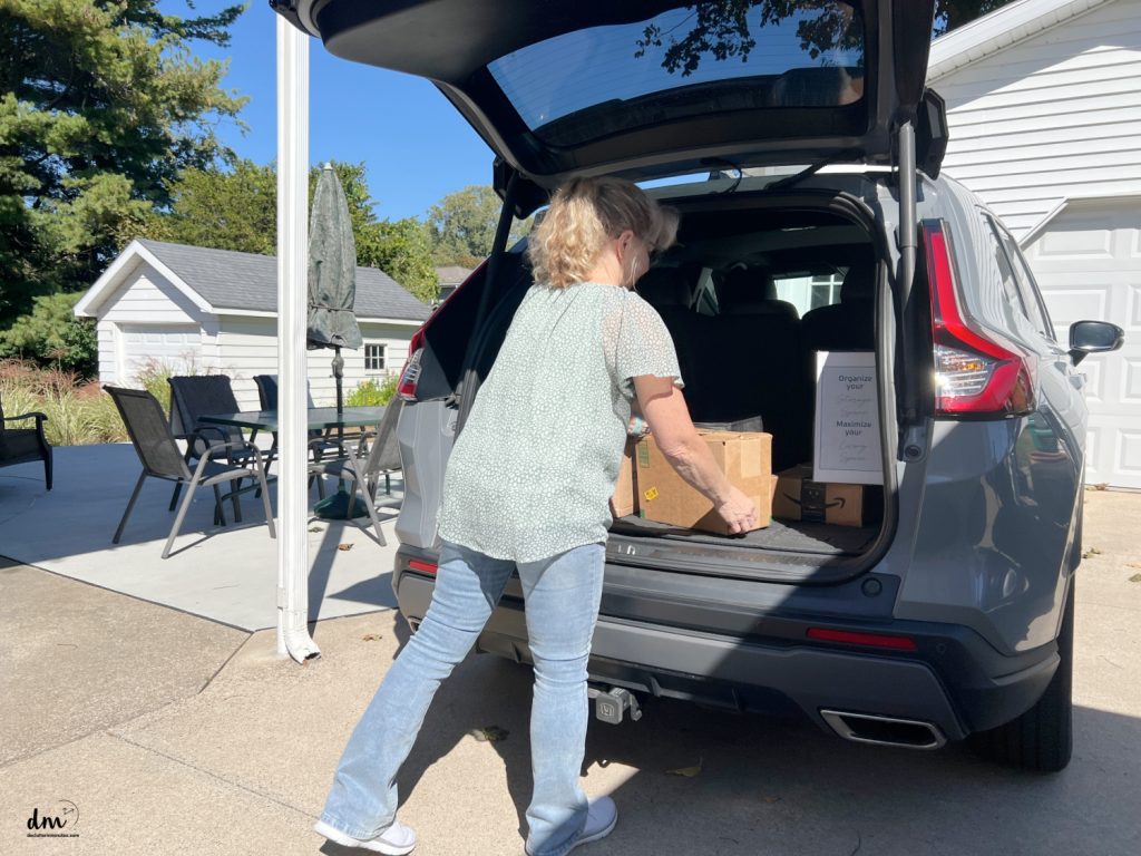 a woman putting donation boxes into the back of her car