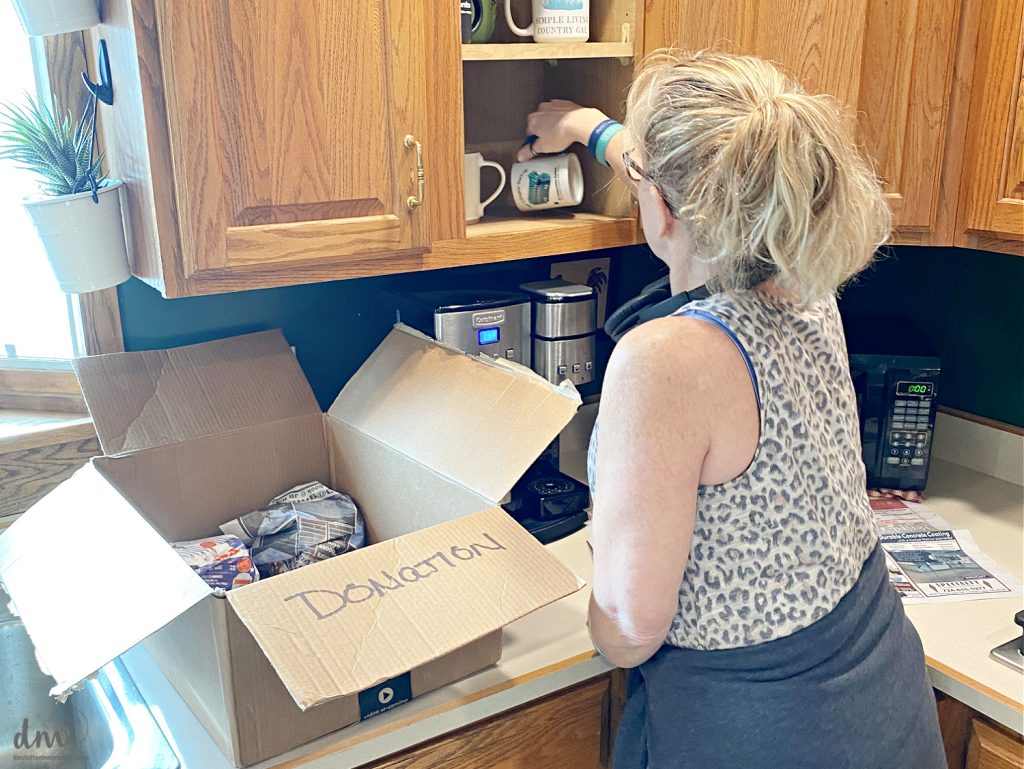 hand grabbing a coffee mug next to a donation box in a kitchen
