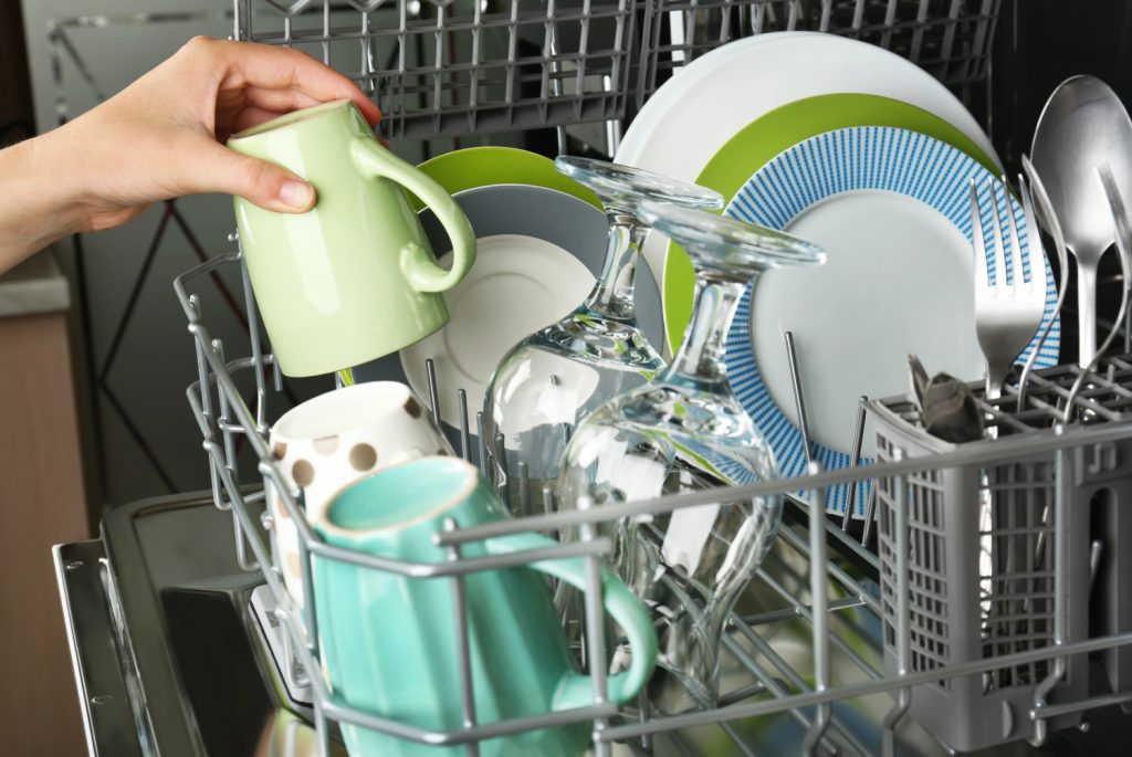 hand putting a green coffee mug into a dishwasher