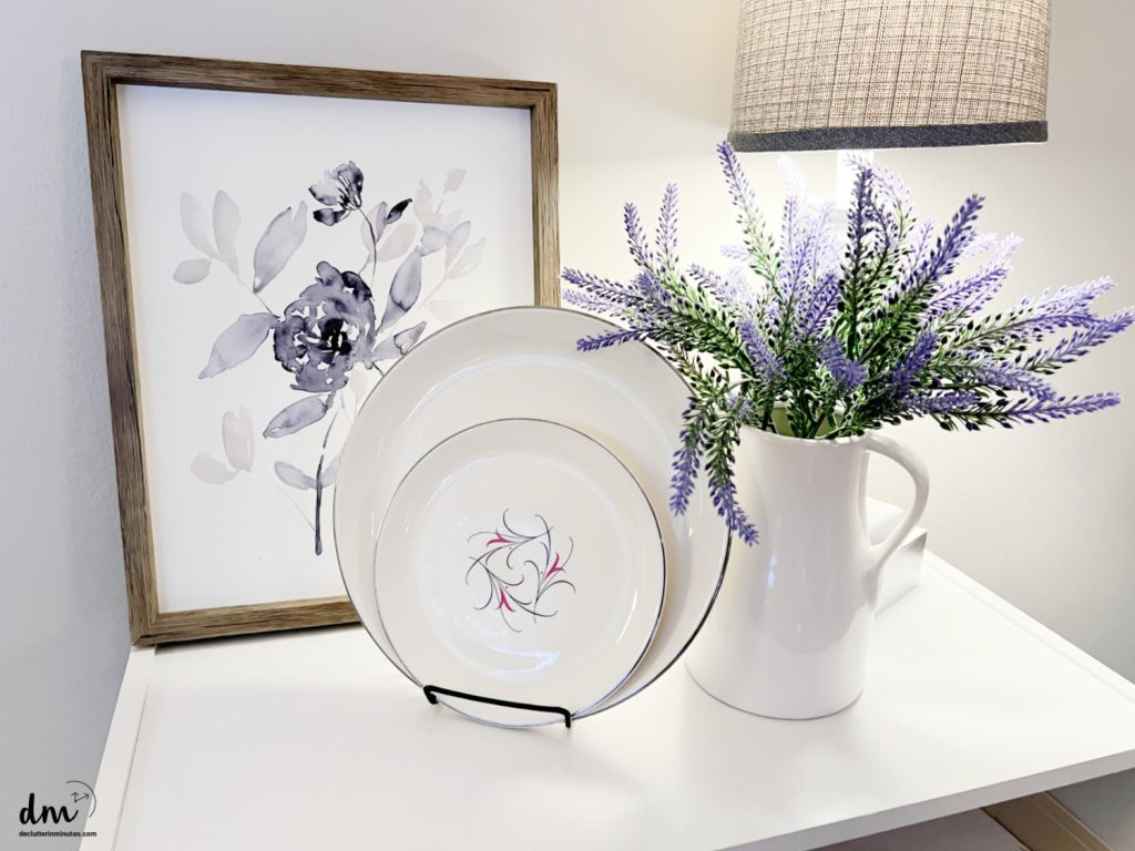plates on a stand on a white table with a vase of flowers and photo