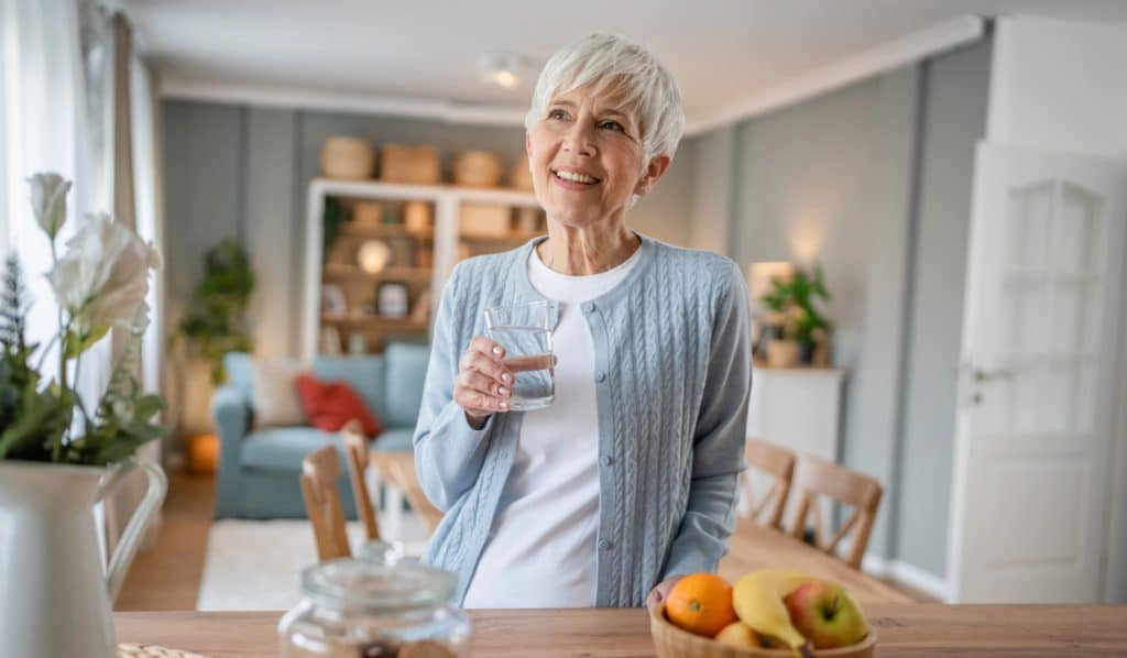 a mature women drinking water in a downsized kitchen