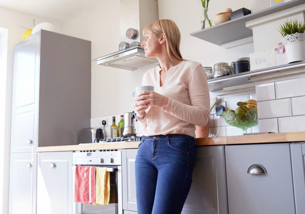 a woman standing in her kitchen drinking coffee