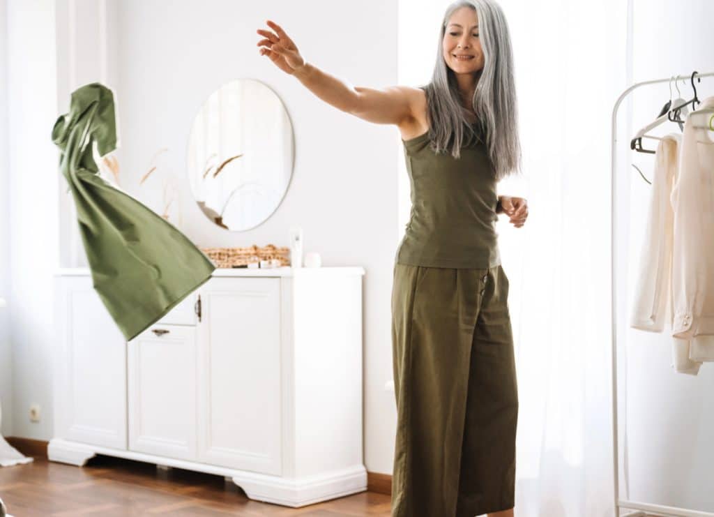 a woman tossing a green dress off to the side for donation