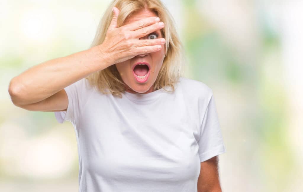 midlife woman covering her face with a hand peaking through her fingers