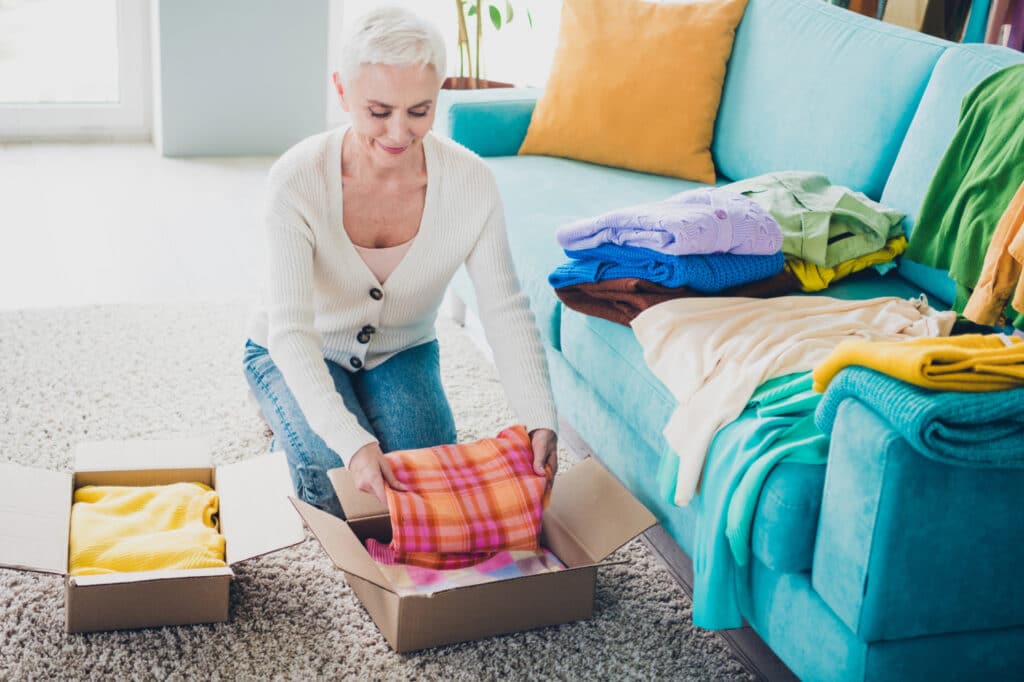 senior woman putting clothes into a donate box sitting on the floor